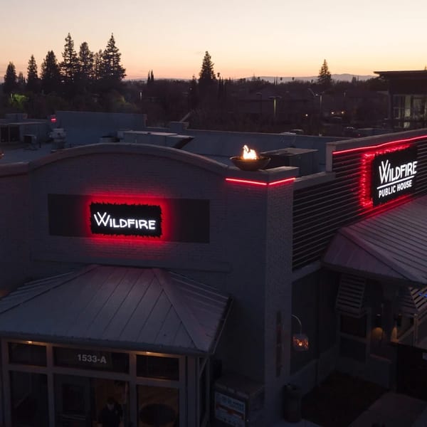 Wildfire Public House exterior at dusk, with glowing red neon signs and a fire pit on the roof.