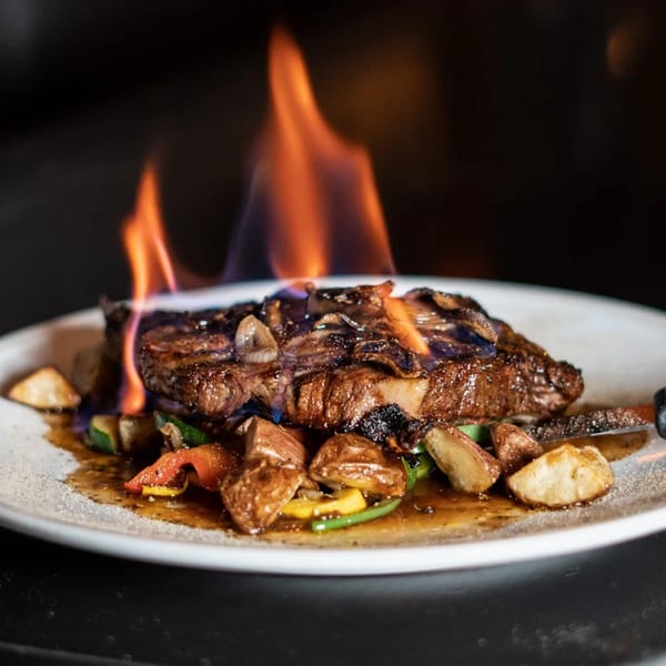 Flaming steak with mushrooms, roasted potatoes, and vegetables on a white plate at Wildfire Public House.