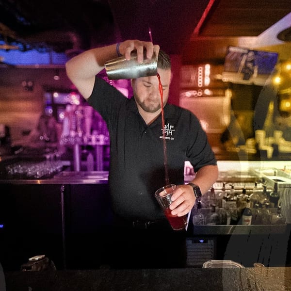 A Wildfire Public House bartender pours a red cocktail from a shaker into a glass.