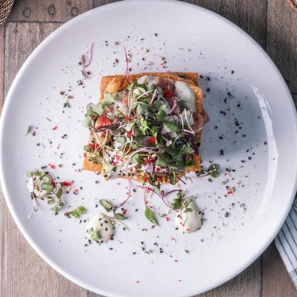 Overhead view of a gastropub dish with microgreens, sauce, and spices on a white plate.