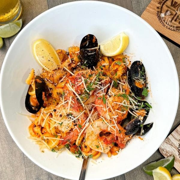 Seafood pasta with shrimp, mussels, and lemon wedges in a white bowl at Wildfire Public House.