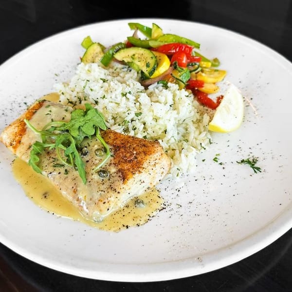 Pan-seared fish with creamy sauce, rice, mixed vegetables, and a lemon wedge on a white plate.