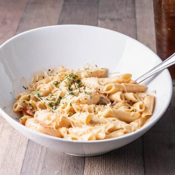 Creamy penne pasta with shrimp, parmesan cheese, and parsley in a white bowl at Wildfire Public House.