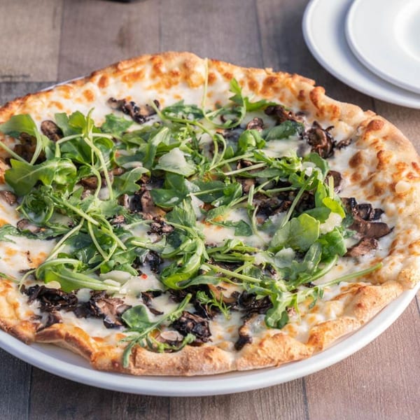Wildfire Public House's mushroom and arugula pizza, with melted cheese and a golden crust, on a white plate.