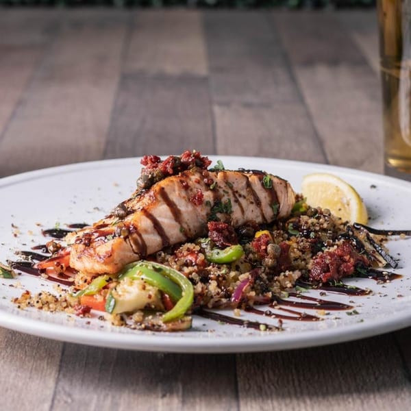 Grilled salmon with quinoa, vegetables, and balsamic glaze, served with a lemon wedge.