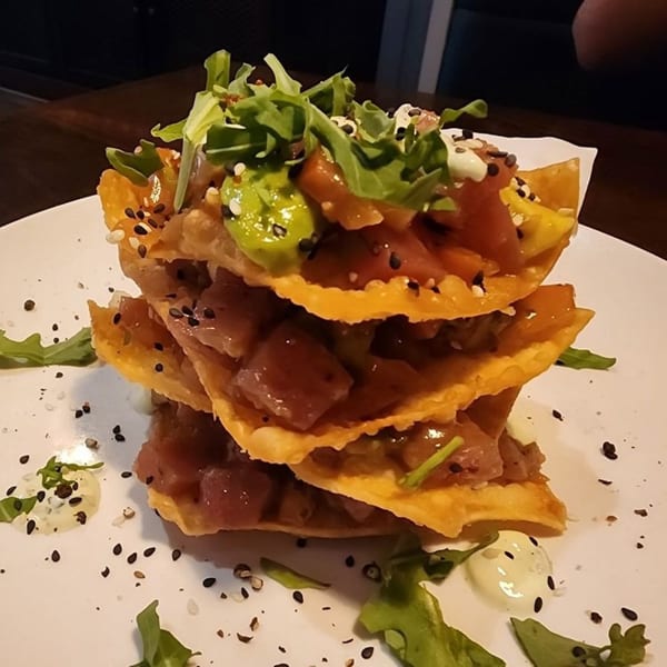 Stacked tuna poke nachos with avocado, arugula, and sesame seeds on a white plate.