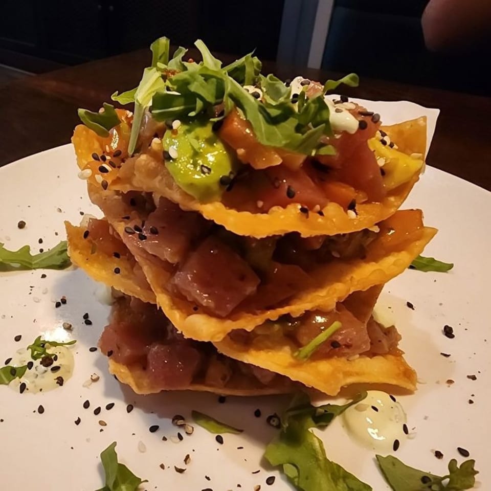 Stacked tuna poke nachos with avocado, arugula, and sesame seeds on a white plate.