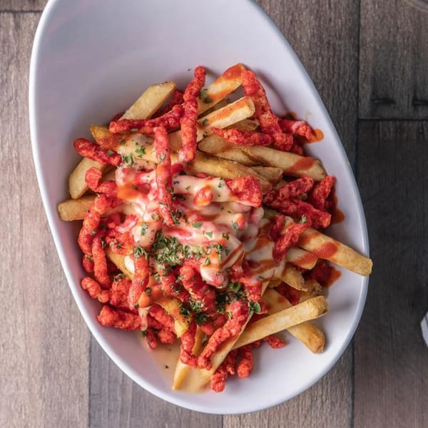 A white bowl filled with golden fries, melted cheese, red hot Cheetos, and green herbs.
